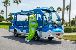 A mascot in a green frog costume standing next to a blue and white bus. - Peaceful Penthouse with Gulf Views! Complimentary Boat Slip! (Orange Beach)