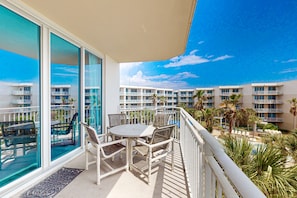 Enjoy a poolside view from this balcony with a table and chairs.