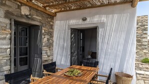A wooden dining table with chairs, a basket, and a door leading to an interior space. - Sky 3 Bedroom Villa Sea View Private Pool (Paros)
