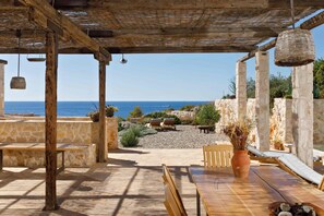 Un patio al aire libre con paredes de piedra, muebles de madera y vista al mar.