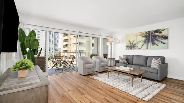 A modern living room with a grey sofa, two armchairs, a wooden coffee table, and a large window overlooking a cityscape. - Gorgeous 2-bedroom listing! Half-block from Waikiki Beach! (Honolulu)
