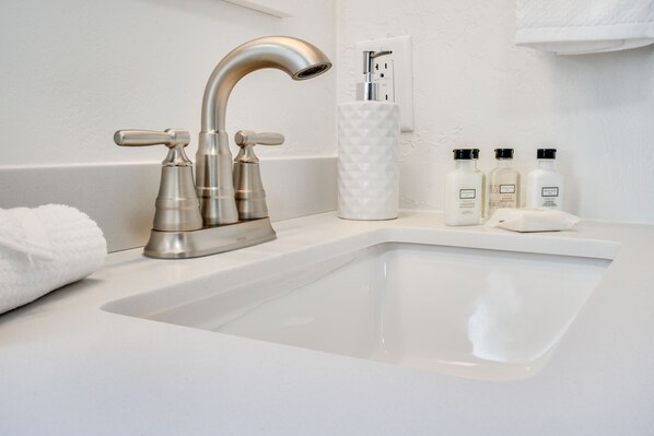 A modern bathroom with a large sink, a curved faucet, and a towel rack. - Gorgeous 2-bedroom listing! Half-block from Waikiki Beach! (Honolulu)
