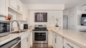 A modern kitchen with white cabinets, stainless steel appliances, and a wooden floor. - Gorgeous 2-bedroom listing! Half-block from Waikiki Beach! (Honolulu)
