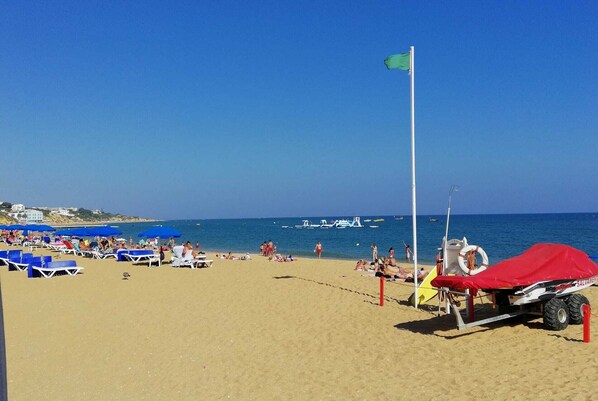 A beach with sun loungers, umbrellas, and a lifeguard stand.