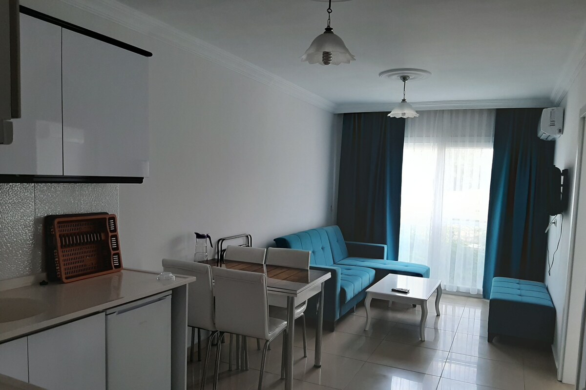 A modern living room with a sofa, a dining table, and a kitchen area with cabinets and a countertop.