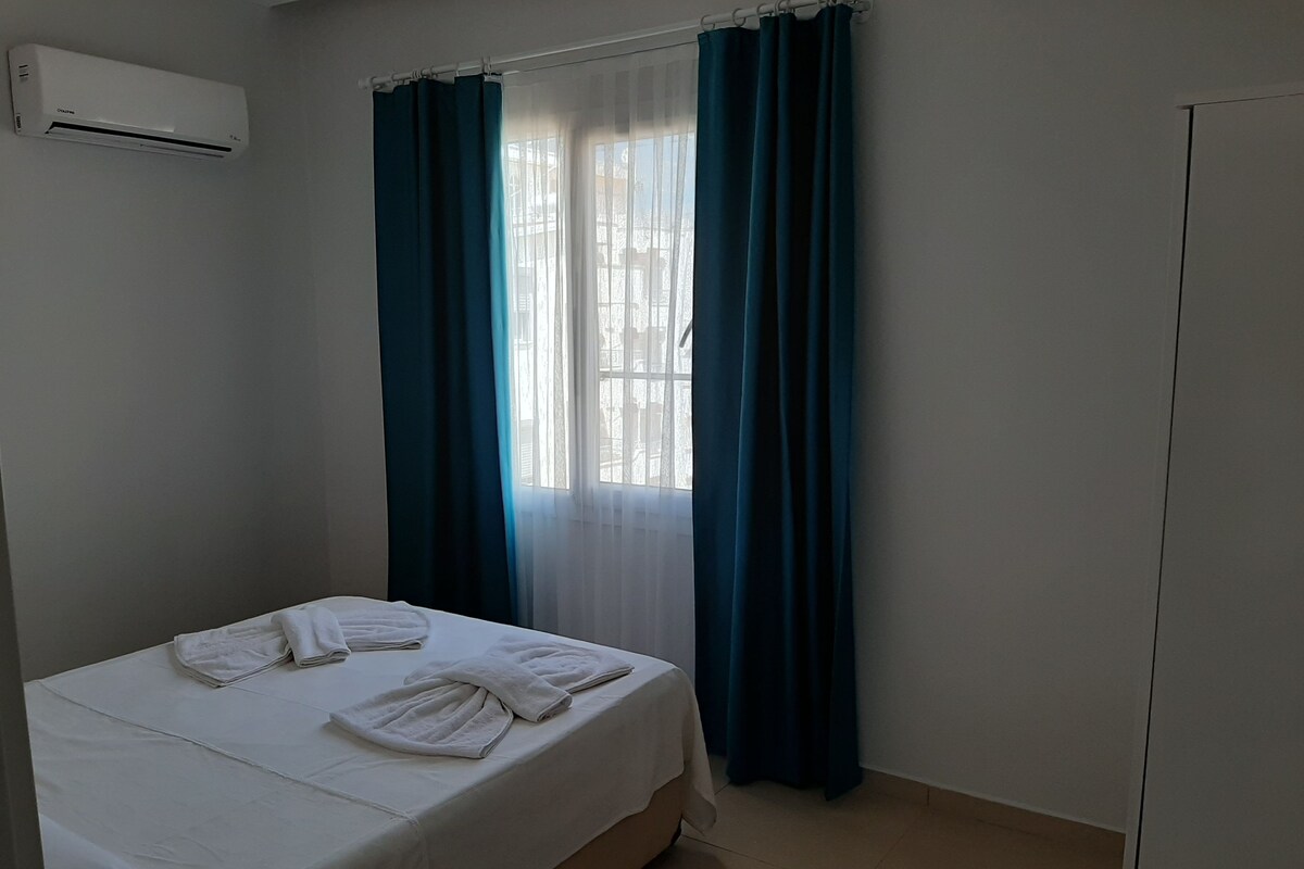 A hotel room with a bed, a window with curtains, an air conditioning unit, and a wardrobe.