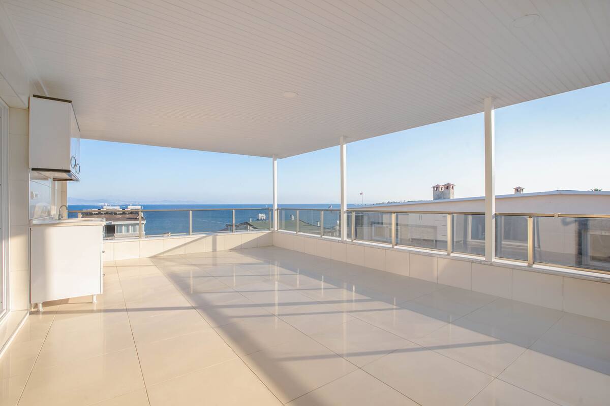A spacious balcony with a view of the sea, a white ceiling, and a kitchen area.