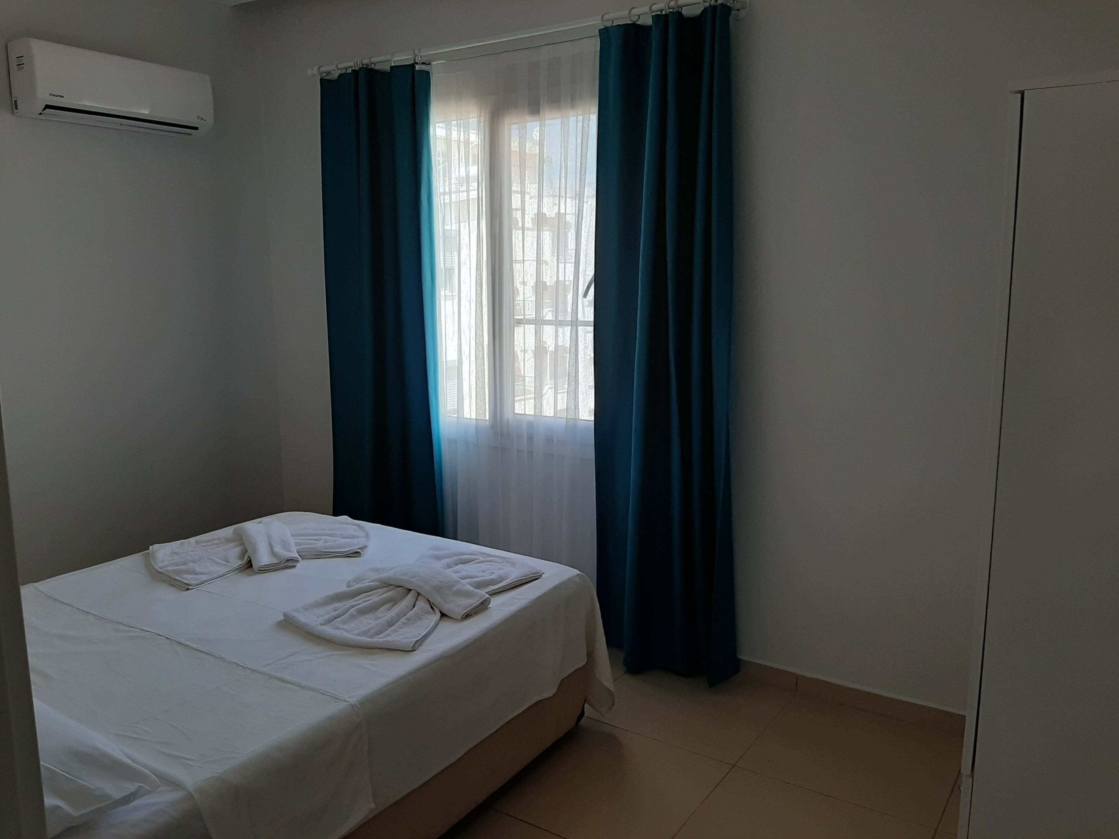 Une chambre d’hôtel comprenant un lit, une fenêtre avec des rideaux, un appareil de climatisation et une armoire.