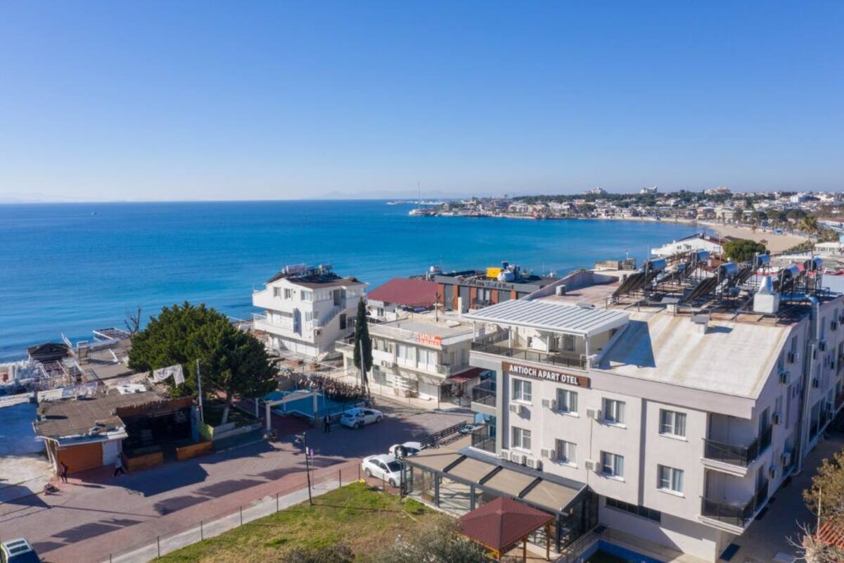 An urban coastal area with a hotel named "ANTIOCH APART HOTEL" featuring a modern design, located near a beach with clear blue waters.