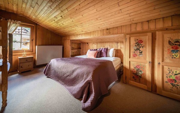 A cozy wooden room with a bed, a nightstand, a radiator, and a window with curtains. - Beau Chalet Savoyard Traditionnel (Morzine)