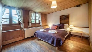 Un dormitorio con paneles de madera, una cama, lámparas de noche, un radiador y una ventana con cortinas.