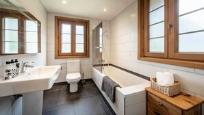 Un baño con inodoro, lavabo y bañera. Cuenta con ventanas y ducha.