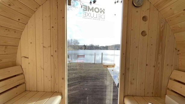 Un sauna aux murs et aux bancs en bois, avec vue sur un lac, et une pancarte indiquant « DOMEN KOBE ».