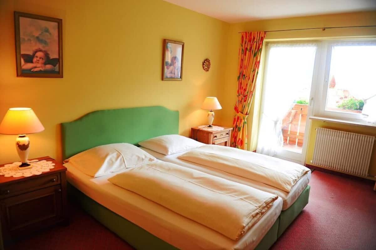 A room with a bed, two bedside tables, a window with curtains, and a radiator.