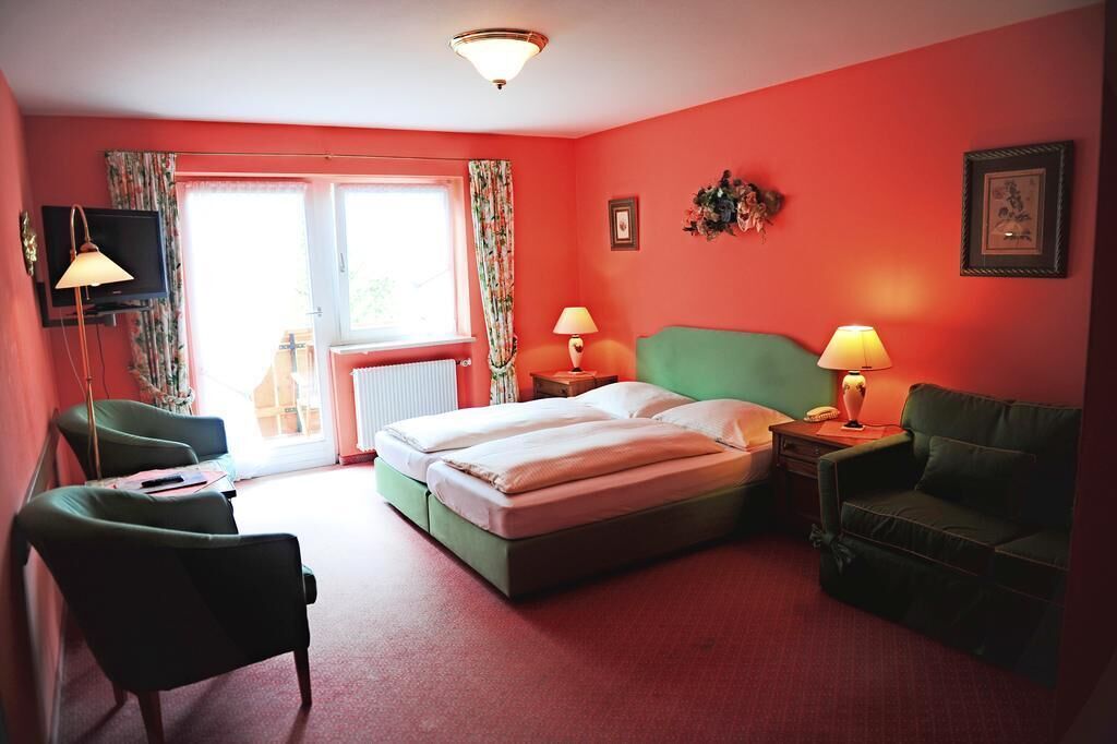 A room with a bed, two chairs, a TV, and a window with curtains.