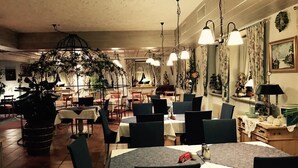 A restaurant with round tables, chairs, hanging plants, and a chandelier. - Hotel Kienberger Hof (Pfronten)