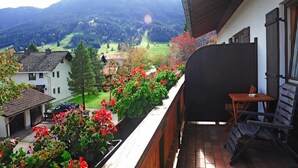 A balcony with a view of a mountainous landscape, a wooden table, and a chair. - Hotel Kienberger Hof (Pfronten)