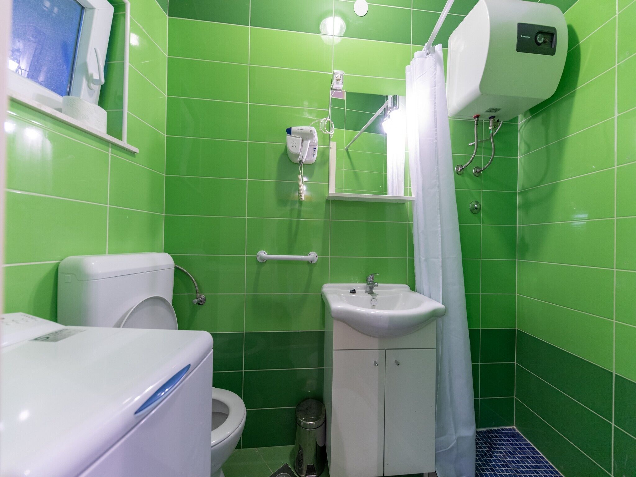 A bathroom with green tiles, a toilet, a sink, a hand dryer, and a shower curtain.