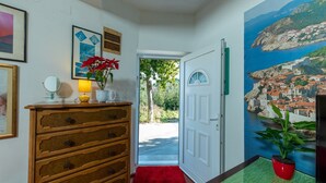 A hallway with a wooden dresser, a red rug, a door leading outside, and a mural of a coastal town.