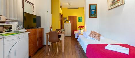 A compact hotel room with a kitchenette, a dining area, and a bed with a red blanket.