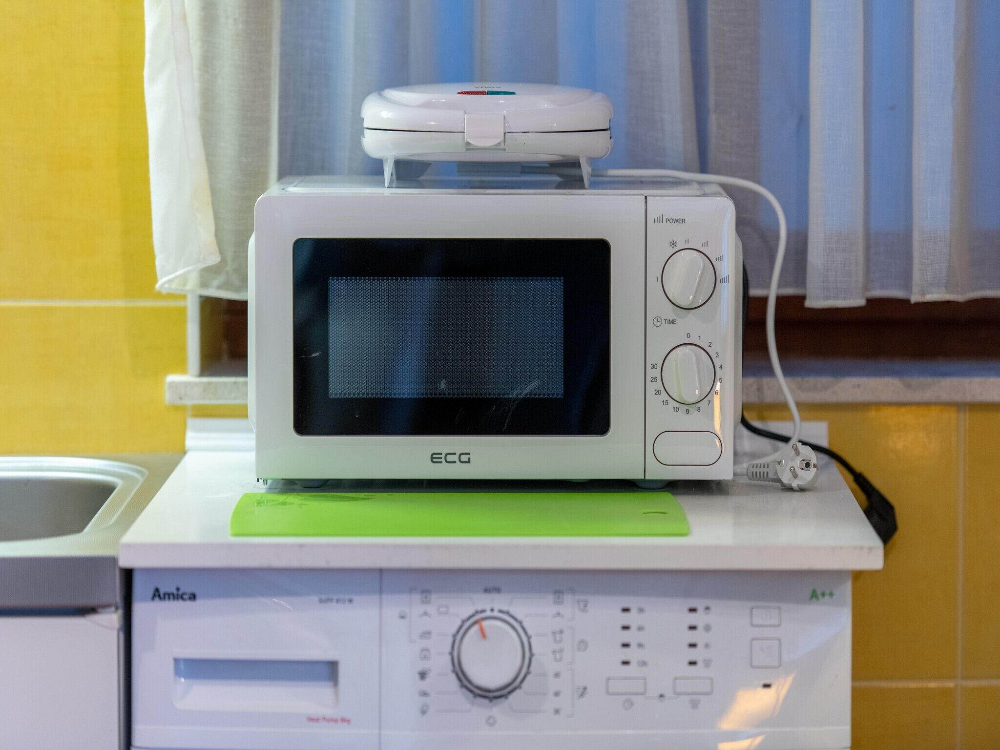 A white ECG microwave oven on a green tray, with a power cord plugged in.