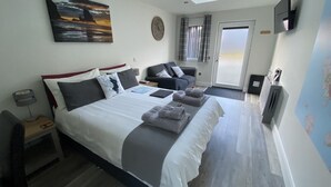 A bedroom with a large bed, a desk, a chair, a TV, and a window with curtains. - Piper's Hut - Central apartment  (Portree)