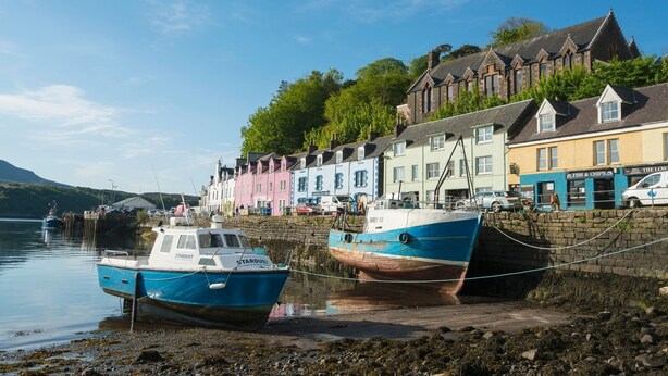 A harbor with boats docked, a stone wall, and colorful buildings along the shore. - Piper's Hut - Central apartment  (Portree)