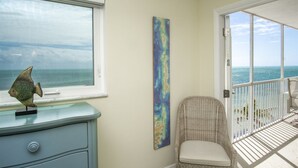 Una stanza con vista sull'oceano, un pesce decorativo sul comodino, una sedia in vimini e un quadro astratto e colorato appeso alla parete.