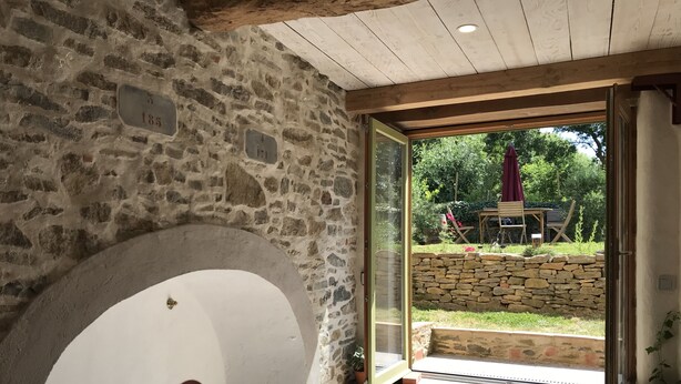 A stone-walled room with a large arched doorway leading to an outdoor patio area. - Renovated wine cellar in the heart of nature (Villetritouls)