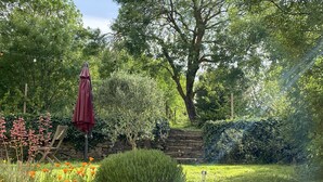 A garden with a stone wall, a wooden bench, and a red umbrella. - Renovated wine cellar in the heart of nature (Villetritouls)