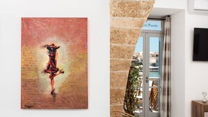 Una pintura de una mujer con un vestido rojo en una pared, una silla de mimbre y una puerta con la leyenda 'Hotel Puerto'.