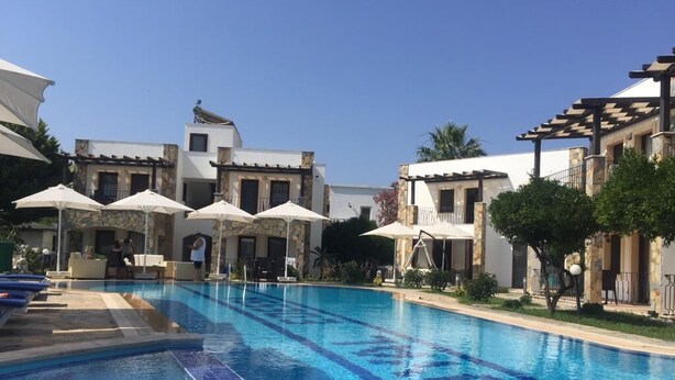 A swimming pool with clear blue water, surrounded by buildings with balconies and outdoor seating areas. - The Mara Suite (Bodrum)