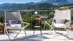 Two wicker chairs with cushions on a balcony with a table and a vase of flowers. The balcony overlooks a mountainous landscape. - Villa Turri is a historic mansion near Lucca in the heart of Garfagnana. (Filicaia)