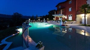 A swimming pool with a curved edge, lounge chairs, and a building with a red facade in the background. - Villa Turri is a historic mansion near Lucca in the heart of Garfagnana. (Filicaia)