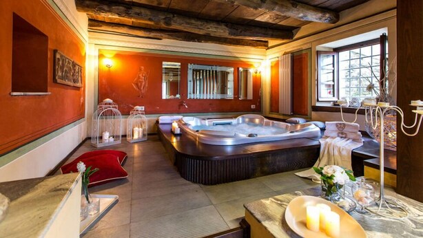 A spa room with a large hot tub, wooden ceiling beams, and a window with a view. - Villa Turri is a historic mansion near Lucca in the heart of Garfagnana. (Filicaia)