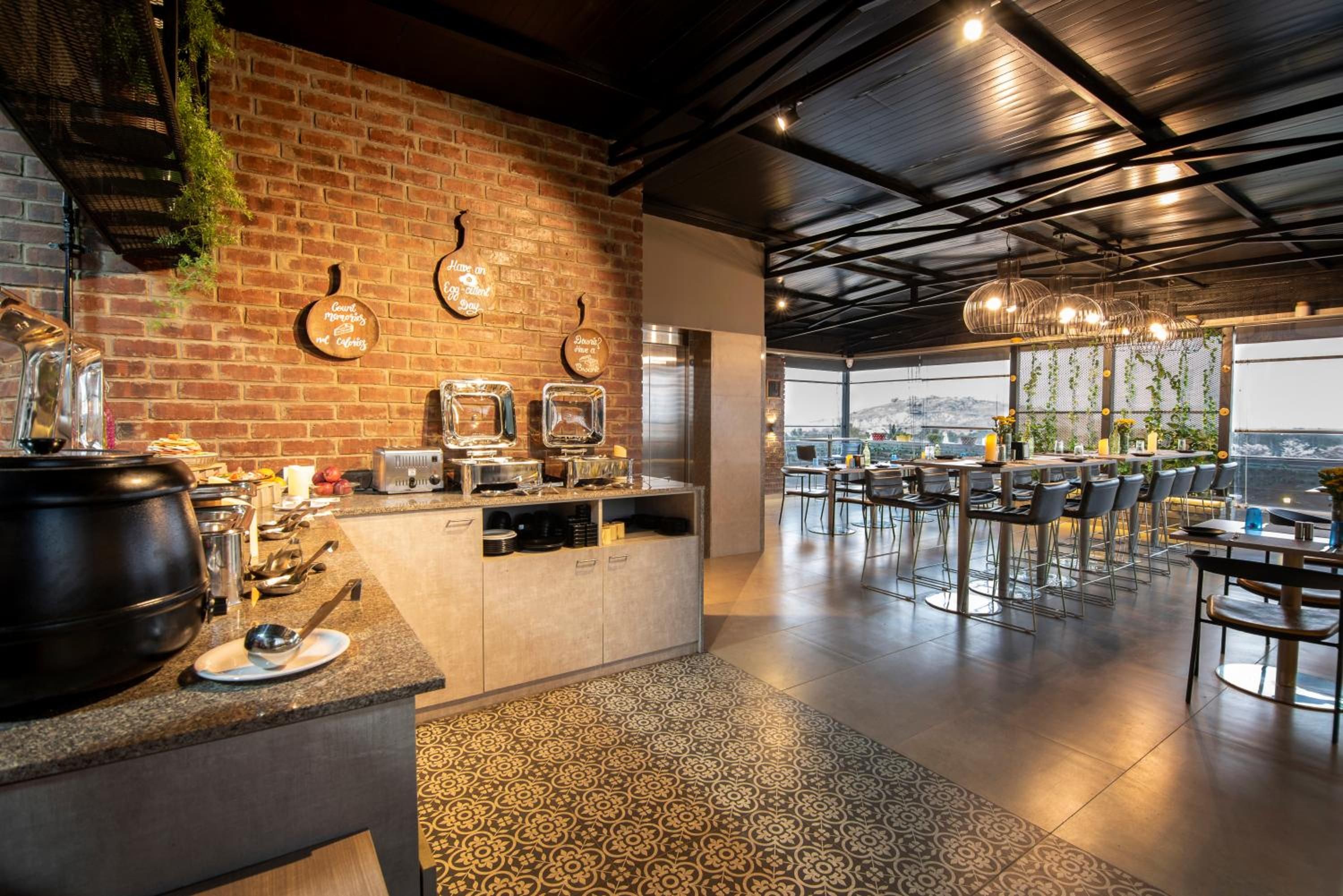 Un restaurant avec un mur en briques, un comptoir où sont exposés divers ustensiles de cuisine, et une salle à manger avec des tables et des chaises.