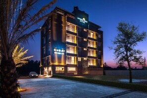 Um hotel de vários andares com design moderno, apresentando um restaurante visível no andar térreo e uma placa indicando área de piscina ao ar livre.
