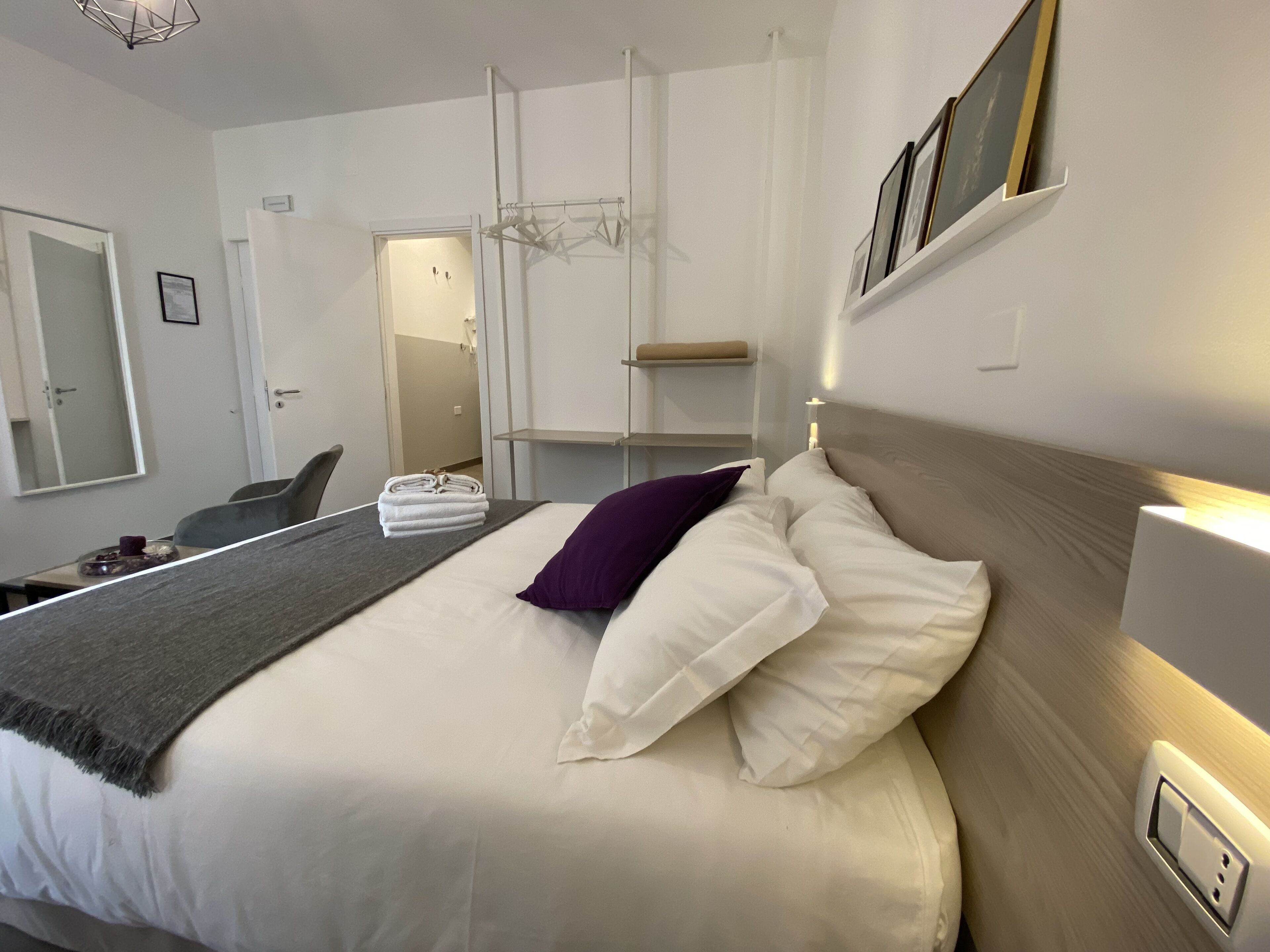 Ein modernes Hotelzimmer mit einem ordentlich bezogenen Bett, einem Sessel, einem kleinen Tisch mit Tasse und Teller sowie einem Spiegel an der Wand.