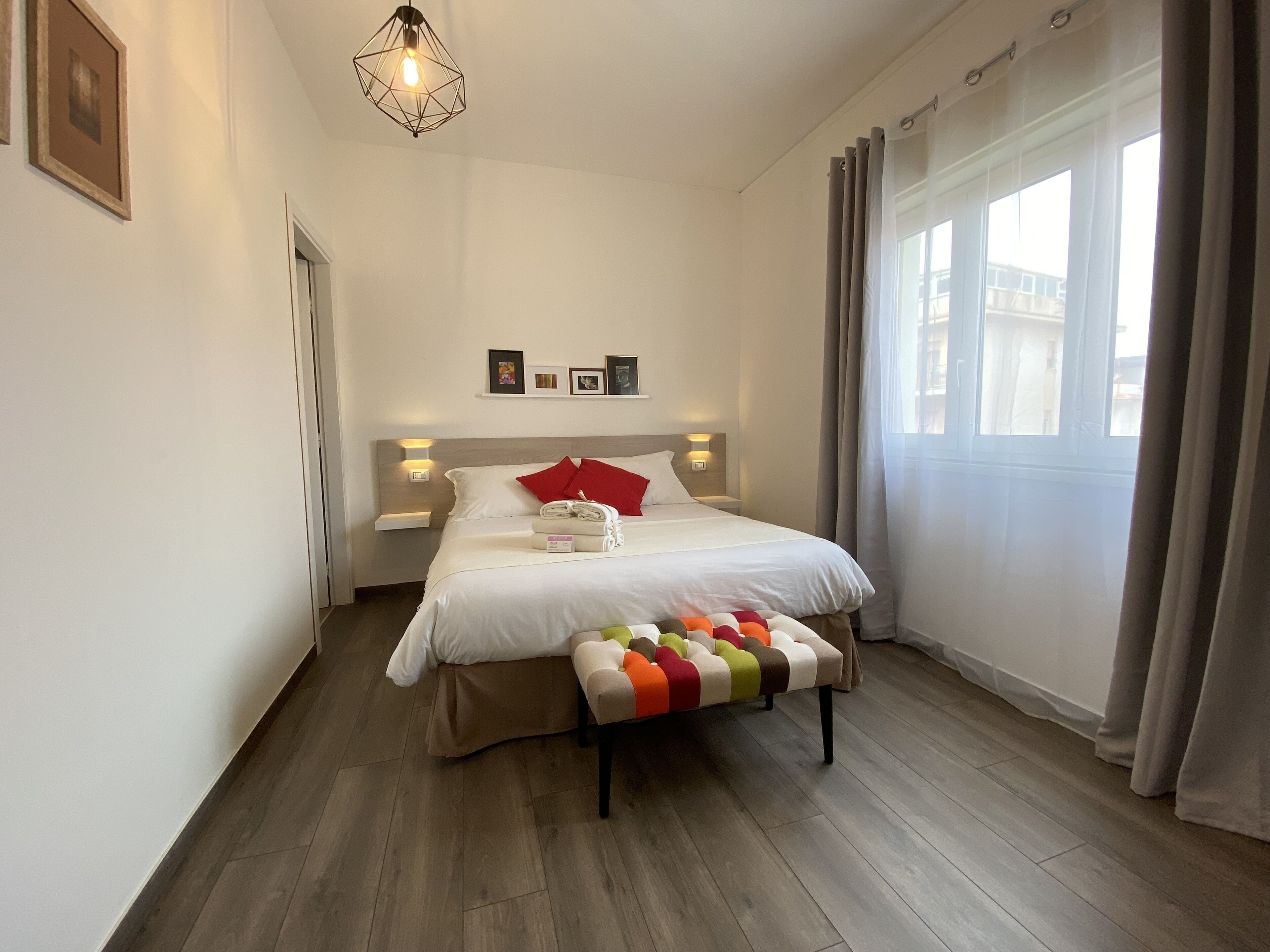 Habitación de hotel ordenada con una cama, mesitas de noche, un banco y una ventana con cortinas.