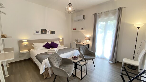 A modern hotel room with a bed, two chairs, a desk, and a lamp. - Ma&Mi Light Rooms (Cefalù)