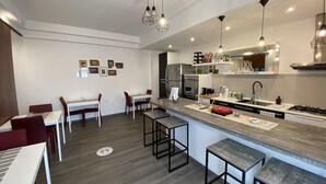 A modern kitchen with a central island, bar stools, and a dining area with red chairs. - Ma&Mi Light Rooms (Cefalù)