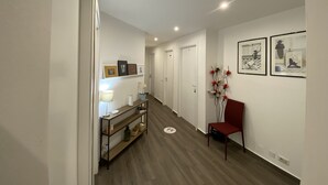 A hallway with a wooden floor, a red chair, a shelf with decorative items, and framed pictures on the wall. - Ma&Mi Light Rooms (Cefalù)
