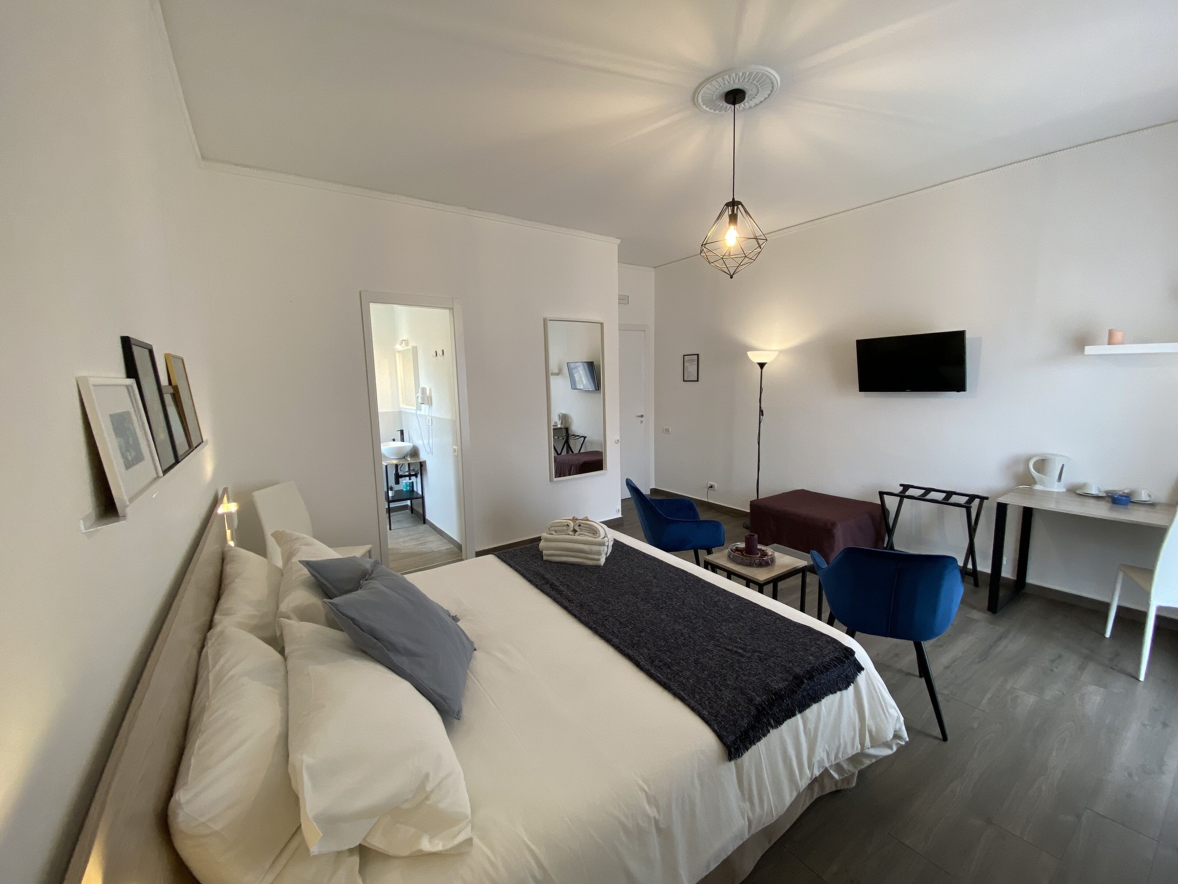 A hotel room with a bed, a desk, a chair, a TV, and a bathroom visible through an open door.