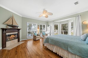 A bedroom with a fireplace, a bed with a blue bedspread, and a ceiling fan. - Waterfront Bay property with private beach and pier! (Gulf Shores)
