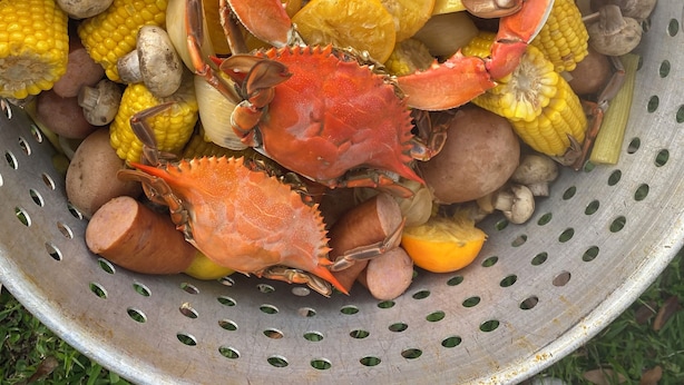 A colander filled with crabs, corn, potatoes, and citrus fruits.