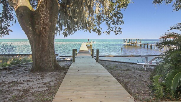 A wooden boardwalk leading to a pier over water, with a tree on the left and a covered area on the right. - Waterfront Bay property with private beach and pier! (Gulf Shores)