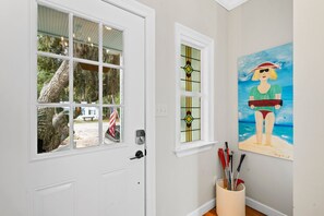 A white door with a view of a tree and a bench outside, a painting of a person on a beach, and a basket with tools on the floor.