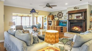A living room with a fireplace, a ceiling fan, and a large window. - Waterfront Bay property with private beach and pier! (Gulf Shores)