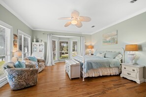 A bedroom with a bed, bedside tables, a chair, a ceiling fan, and a window with curtains.