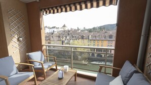 A balcony with wooden furniture, a view of buildings and a bridge, and a tiled floor. - Superbe 120m2 - 2chambres + 2sdb, 3 Grds Balcons (Annecy)